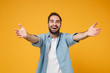© ViDi Studio - Cheerful young bearded man in casual blue shirt posing isolated on yellow orange background studio portrait. People emotions lifestyle concept. Mock up copy space. Standing with outstretched hands.