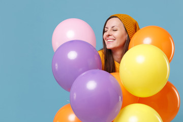 Cute young woman girl in sweater hat posing isolated on blue background. Birthday holiday party people emotions concept. Mock up copy space. Celebrating hold colorful air balloons keeping eyes closed.