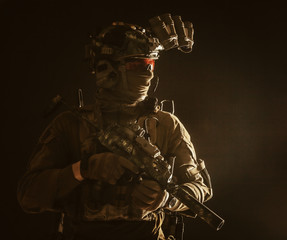 Army special forces tactical group fighter moving in darkness, using radio headset, looking through four lens night-vision, thermal imaging device on helmet, armed small submachine gun with silencer