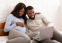 Happy Pregnant Couple Choosing Furniture For Baby Room Online
