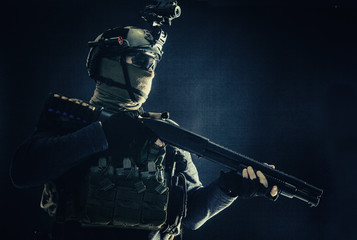 Shoulder portrait of army elite troops soldier, anti-terrorist tactical team wit shotgun, helmet with thermal imager, hiding face behind mask, armed rifle with optical scope, studio shoot on black