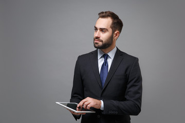 Handsome young business man in suit shirt tie posing isolated on grey background. Achievement career wealth business concept. Mock up copy space. Holding and using tablet pc computer, looking aside.