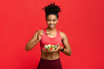 Wall Mural - Healthy sporty girl eating veggies salad over red background