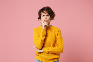 Wall Mural - Displeased pensive young brunette woman girl in yellow sweater posing isolated on pastel pink wall background studio portrait. People lifestyle concept. Mock up copy space. Put hand prop up on chin.
