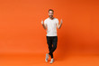 Cheerful excited young man in casual white t-shirt posing isolated on bright orange wall background studio portrait. People sincere emotions lifestyle concept. Mock up copy space. Showing thumbs up.