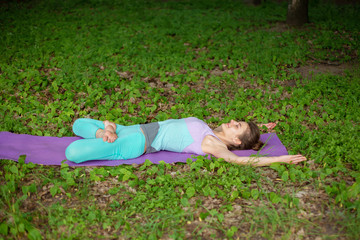 A young sports girl practices yoga in a quit green summer forest, yoga assans posture. Meditation and unity with nature