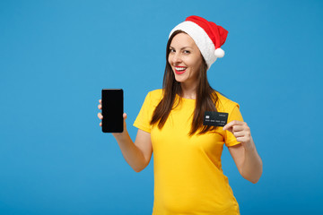 Wall Mural - Smiling woman Santa girl in Christmas hat posing isolated on blue background. New Year 2020 celebration holiday concept. Mock up copy space. Hold credit bank card mobile phone with blank empty screen.