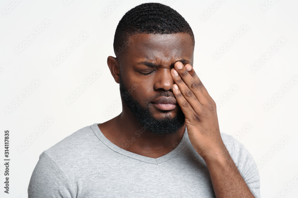 Sad black guy touching his eye, suffering from conjuctivitis - obrazy, fototapety, plakaty 