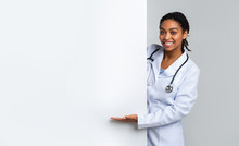 Black Muslim Female Doctor Pointing At White Advertisement Board, Presenting Something