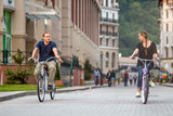 Fototapeta  - Happy smiling Caucasian family of father, mother and daughter have outdoor bicycle ride at summer on hotel buildings background. Active leisure and sport activities at resort.