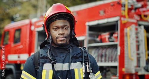 Portrait of african american Firefighter in uniform and helmet near fire engine Poster Mural XXL