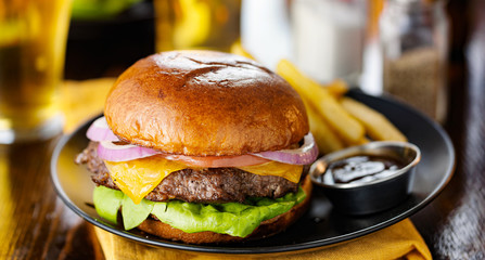 cheeseburger and fries on plate served with beer at restaurant