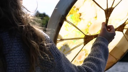 Wall Mural - A short movie showing close up details of a person playing a scared drum, native powwow handcrafted artifact with stretched rawhide membrane, backlit