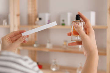 Woman with bottle of perfume and blotter indoors, closeup