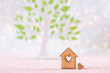Wooden icon of house with hole in form of heart with green tree on white background with bokeh lights.