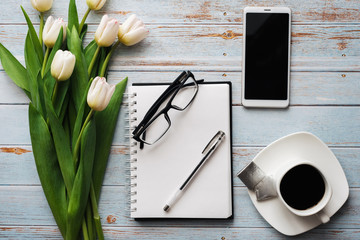 Wall Mural - White bouquet of tulips on wooden background with coffee Cup, smartphone and empty notebook