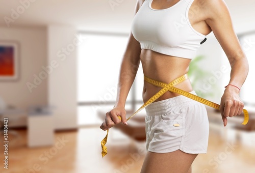 Cuadros en Lienzo Young woman measuring her waist on an interior background