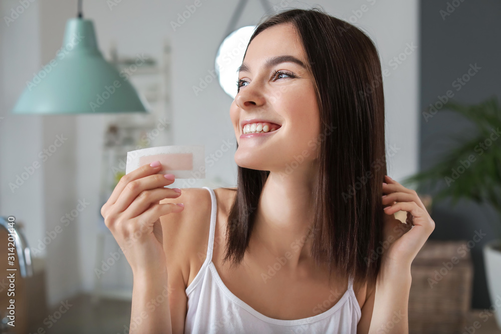 Beautiful young woman with wax strip in bathroom