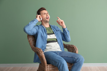 Poster - Handsome man listening to music while sitting in armchair near color wall