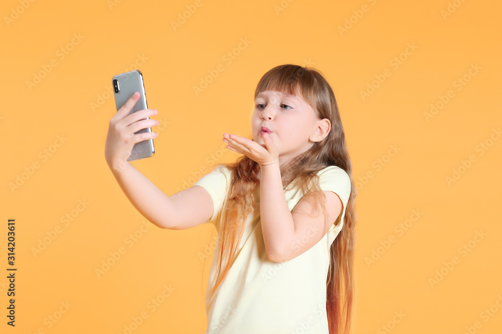 Cute little girl taking selfie on color background