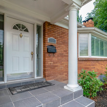 Square Facade Of Home With Brick Exterior Wall Porch Bay Windows And White Front Door