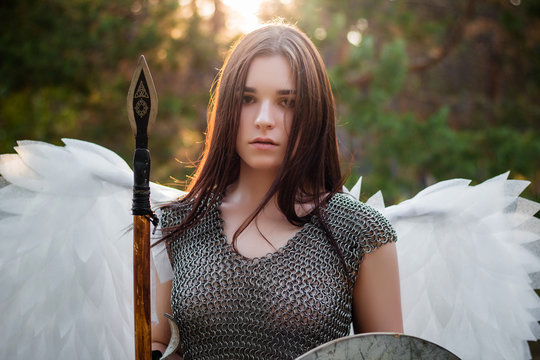 Portrait of a warrior woman in chain mail with steel bracers and wings behind her back. Standing in a fighting position with a spear and a shield in his hands.