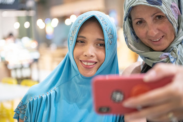 Poster - Muslim women wearing Hijab smiling taking selfies in a city mall