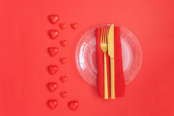 Wall Mural - Gold cutlery on crystal plate and red hearts on red background with monochromatic effect. Saint Valentines day celebration or romantic dinner concept.