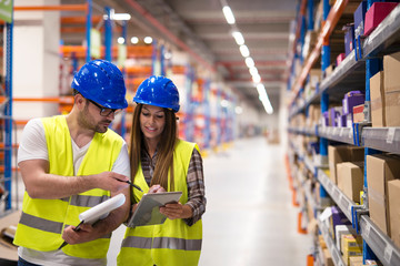 Warehouse workers checking inventory and consulting each other about organization and distribution of goods. Teamwork at warehouse storage department.