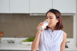 © makistock - Portrait of young Asian woman drinking milk while standing in the kitchen.