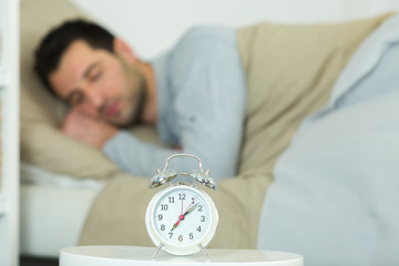 alarm clock with sleeping man on bed