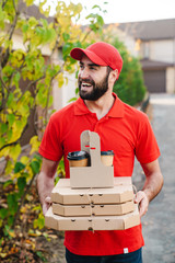 Canvas Print - Image of smiling young delivery man holding pizza boxes and coffee