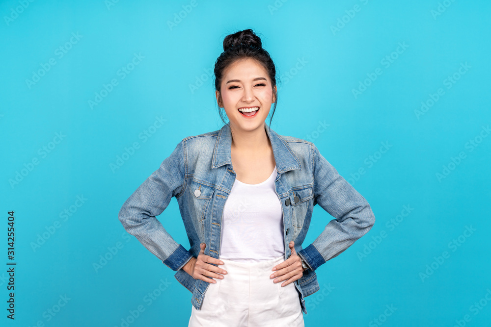 Portrait of Happy asian woman standing and feeling happiness and confident on blue background. Cute asia girl smiling or laughing wearing casual travel uniform in jeans shirt and keeping hands on hips - obrazy, fototapety, plakaty 