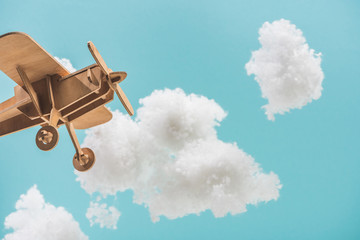 Wall Mural - wooden toy plane flying among white fluffy clouds made of cotton wool isolated on blue