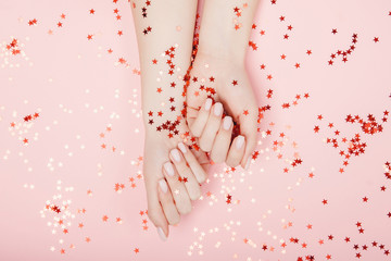 Wall Mural - Stylish trendy nail young woman hands pink manicure on background with red star confetti, top view. Concept skin care spa