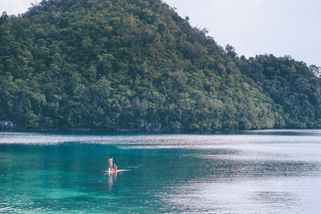 Wall Mural - Summer holidays vacation travel. SUP Stand up paddle board. Young women sailing together on beautiful calm lagoon.