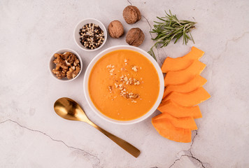 Wall Mural - Pumpkin soup with walnuts in white bowl decorated with pumpkin slices and spices top view on white marble background