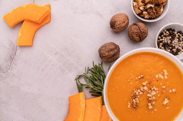 Wall Mural - Pumpkin soup with walnuts in white bowl decorated with pumpkin slices and spices top view on white marble background with copy space