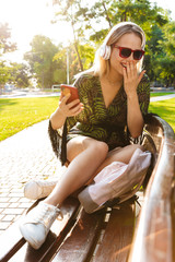 Canvas Print - Beautiful happy young blonde woman sitting on a bench