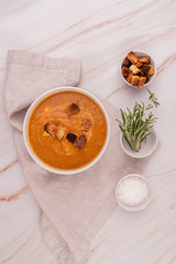 Wall Mural - Pumpkin soup with croutons in white bowl with salt, rosemary and dried bread top view flat lay