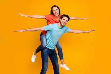 Poster - Photo of two funny people guy carry lady piggyback meet summer time together spread hands like wings wear casual stylish blue orange t-shirts jeans isolated yellow color background