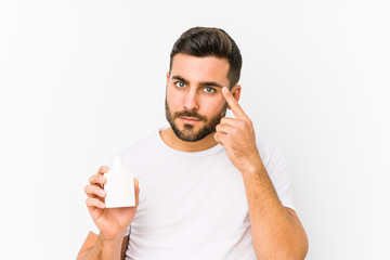 Young caucasian man holding a vitamins bottle isolated pointing his temple with finger, thinking, focused on a task.