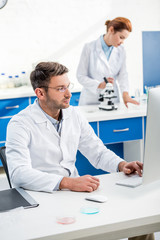 Wall Mural - selective focus of molecular nutritionist using computer and his colleague using microscope on background