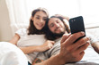© Drobot Dean - Loving couple indoors at home lies using mobile phone together.