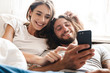 © Drobot Dean - Loving couple indoors at home lies using mobile phone together.