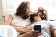 © Drobot Dean - Loving couple indoors at home lies using mobile phone together.