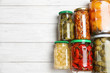 Glass jars with different pickled vegetables on white wooden table, flat lay. Space for text