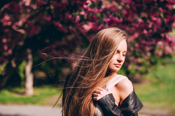 Wall Mural - A close-up portrait of a blonde girl against the backdrop of a Japanese flowering tree of sakura. A beautiful young woman with long blond hair in the spring park.