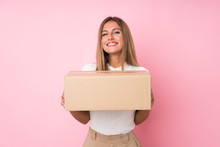 Young Blonde Woman Over Isolated Pink Background Holding A Box To Move It To Another Site