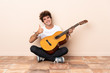 © luismolinero - Young caucasian man with a guitar sitting on the floor with thumbs up because something good has happened